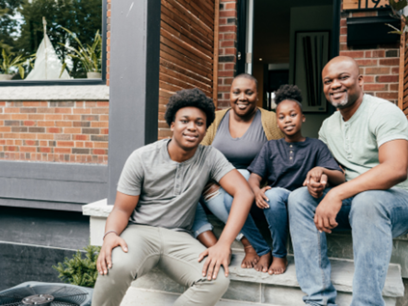 smiling family of four sitting on front porch with door open behind them