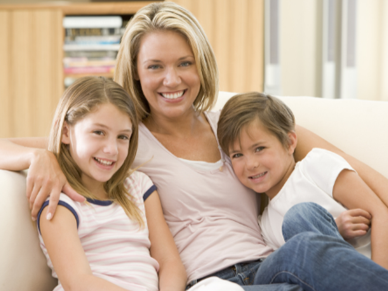 woman with two children, smiling, sitting on sofa at home